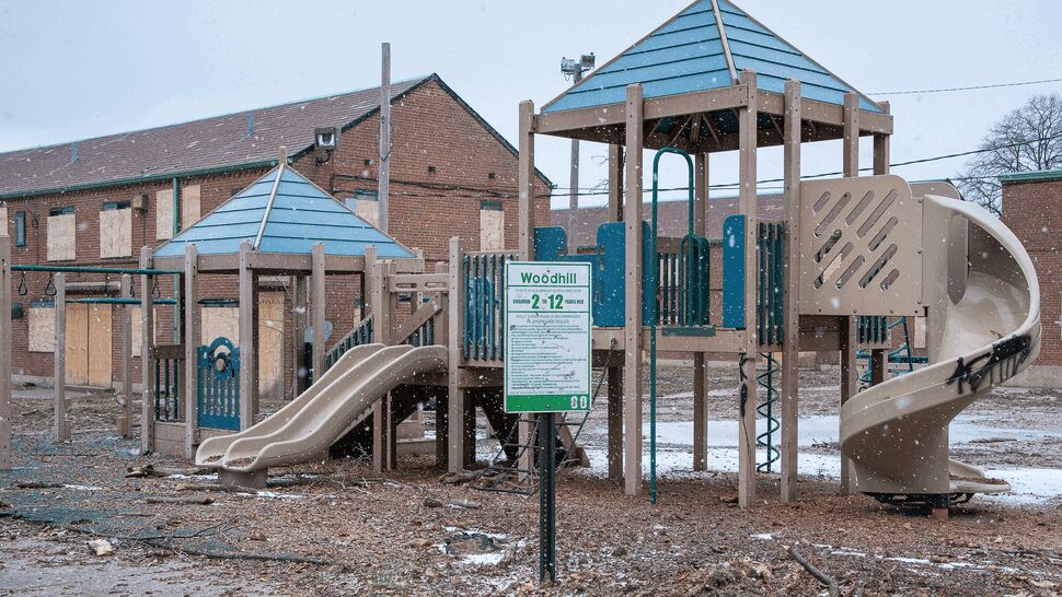 Snow-dusted playground with boarded windows and plastic slides in front of brick buildings