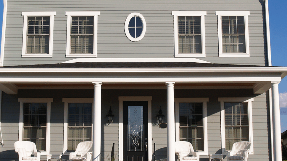 Gray two-story house with white columns, black front door, and porch seating