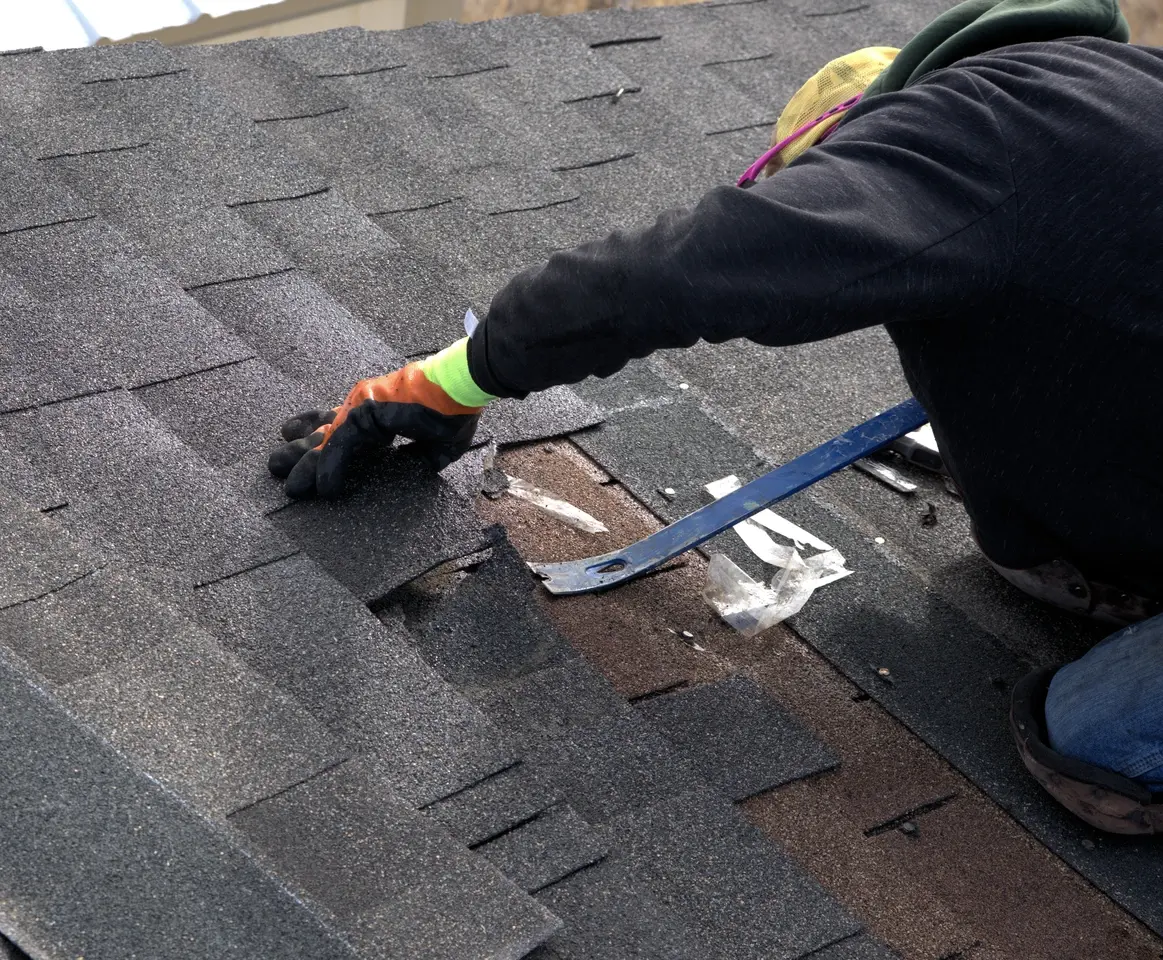 Close up view of roofing contractor using pry bar to removed damaged roof shingles