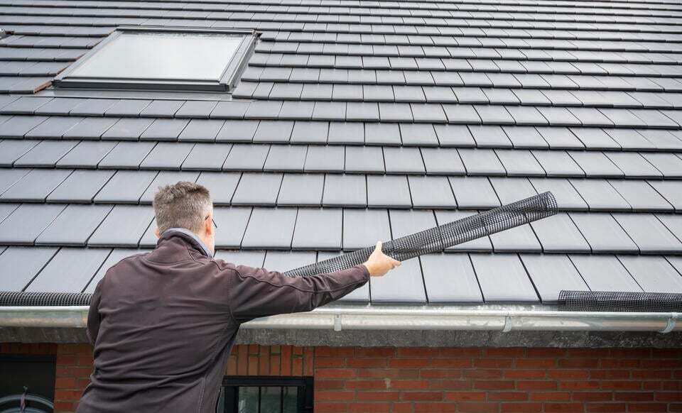diy gutter guards-man installing a roll of mesh into a gutter system