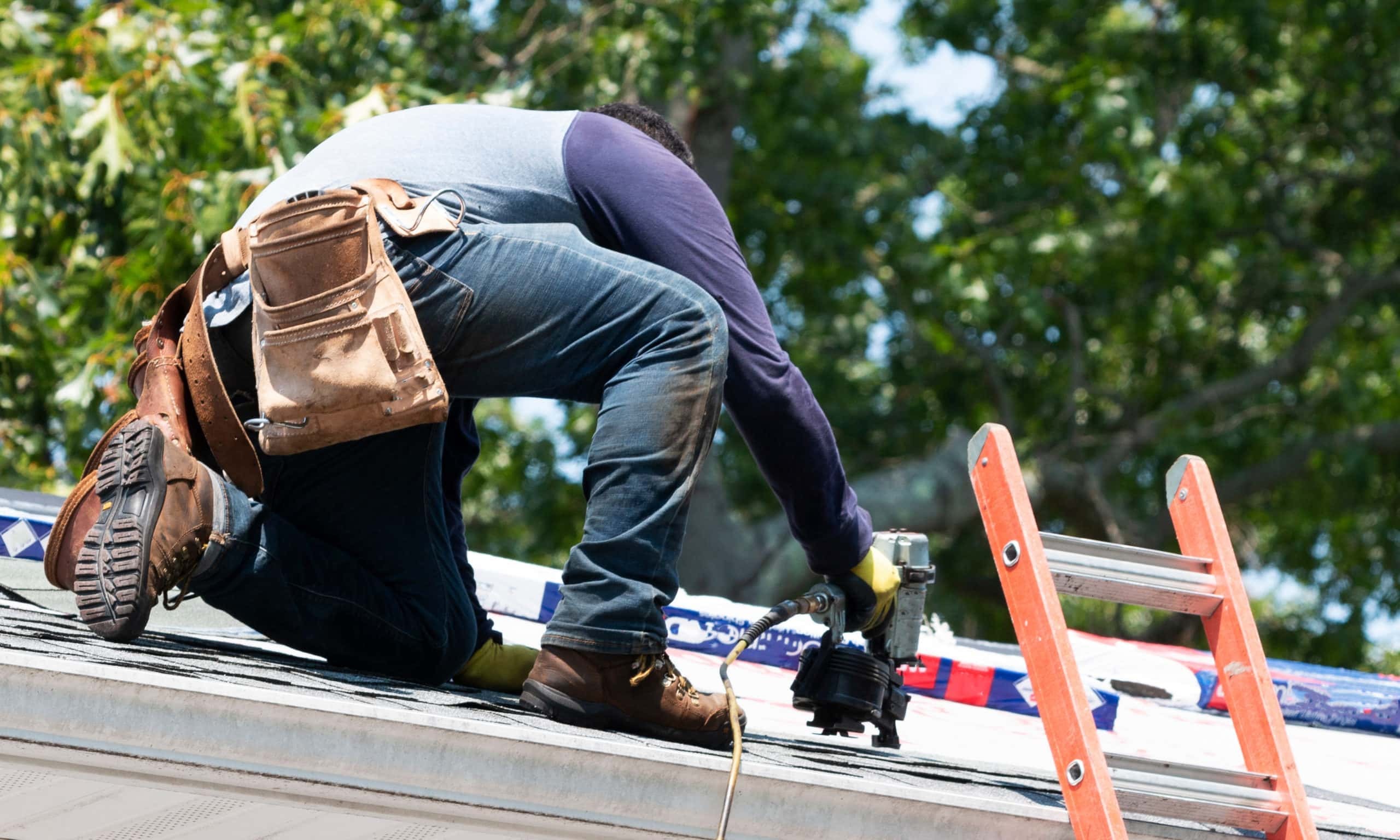 man on roof using nail gun showing when to replace roof