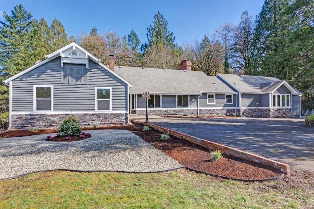 Large one story home exterior with manicured front yard, gray wood and stone siding.