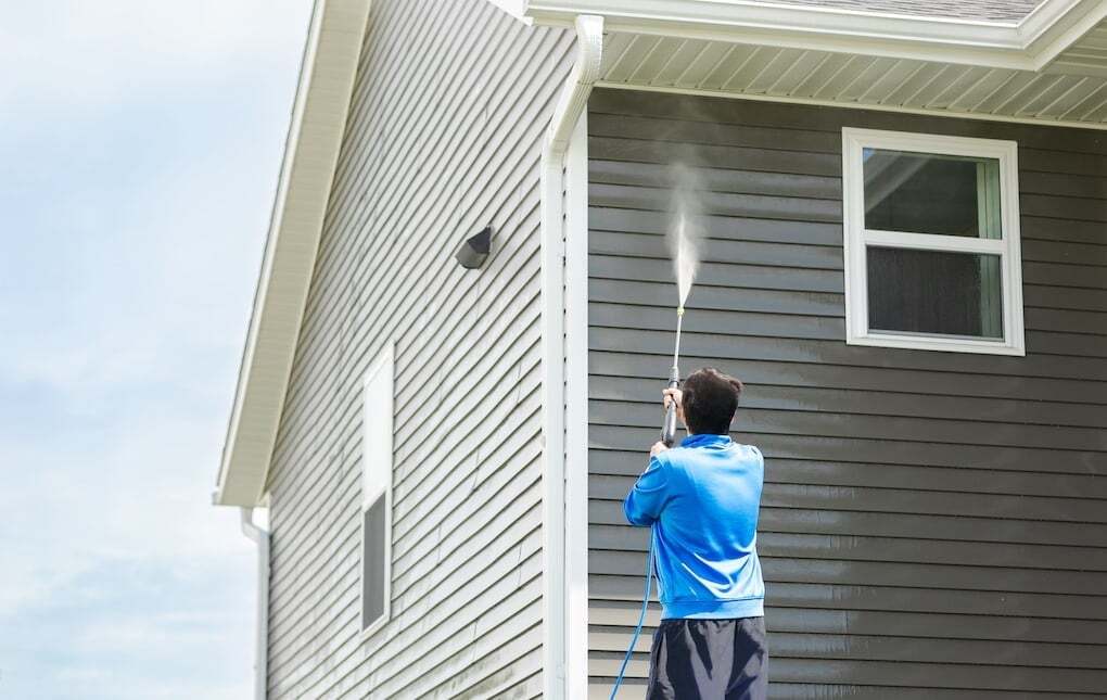 man in blue jacket power washing siding on home: james hardie siding installation