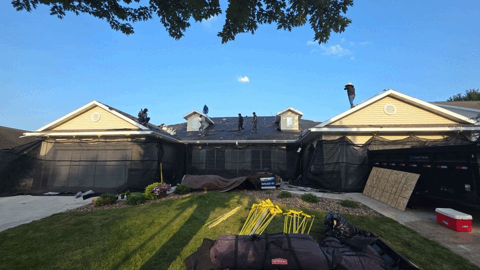 Active Roof Replacement Crew | First American Roofing & Siding Inc Crew on roof removing old shingles with supplies staged on lawn