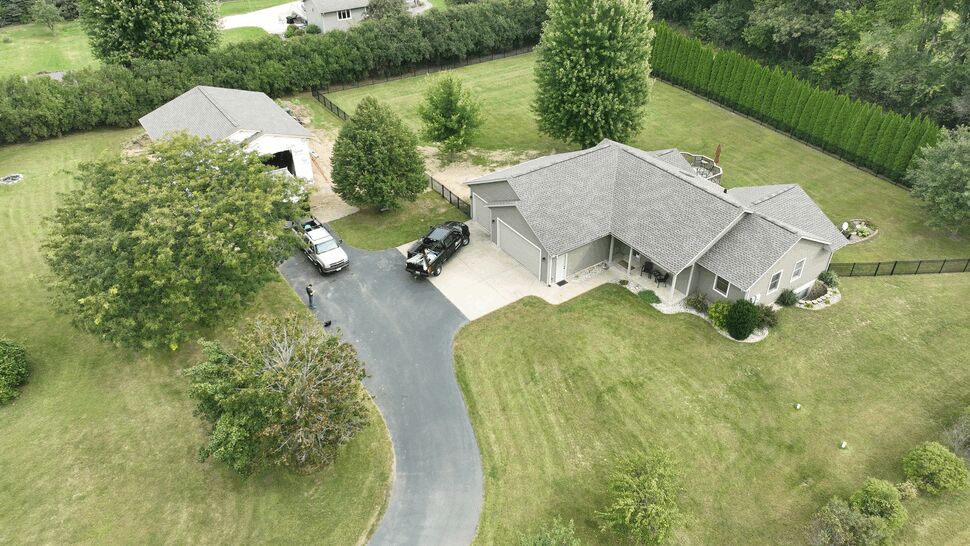 Aerial view of home roof and yard | First American Roofing & Siding Inc Aerial view of a home with gray shingle roof, driveway, vehicles, and surrounding lawn.
