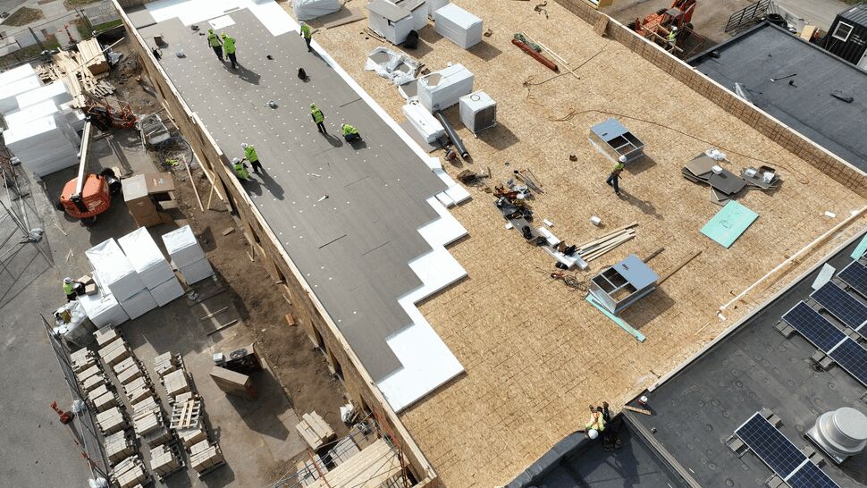Aerial view of crews installing membrane and insulation boards on a large roof.