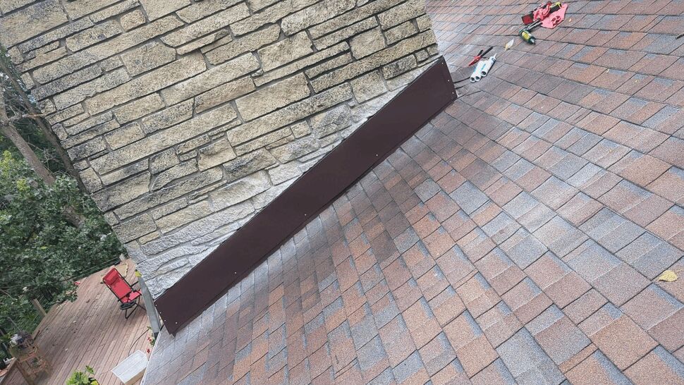 Close view of newly installed apron flashing at chimney base on brown shingle roof with tools