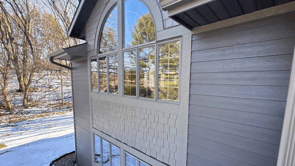 Close-up of arched window and gray siding on two-story home.