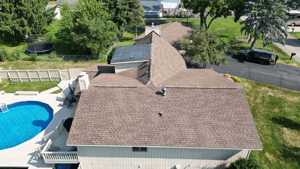 Overhead shot of home roof next to backyard pool and deck with surrounding trees.