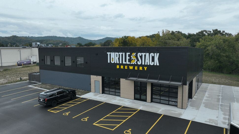 Commercial Brewery Exterior | First American Roofing & Siding Inc Commercial brewery building with a dark facade, parking lot, and mountain backdrop.
