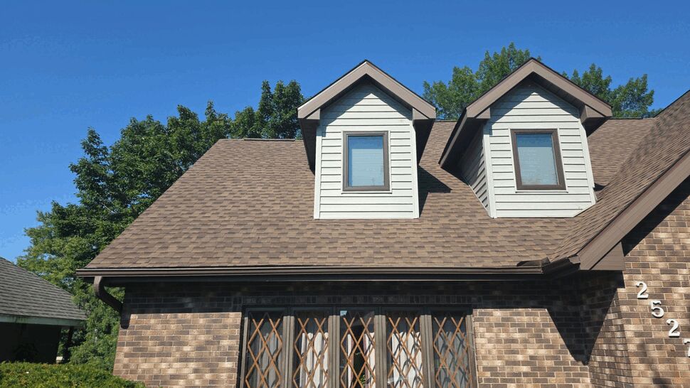 Front of brick house with two dormers and brown shingle roof