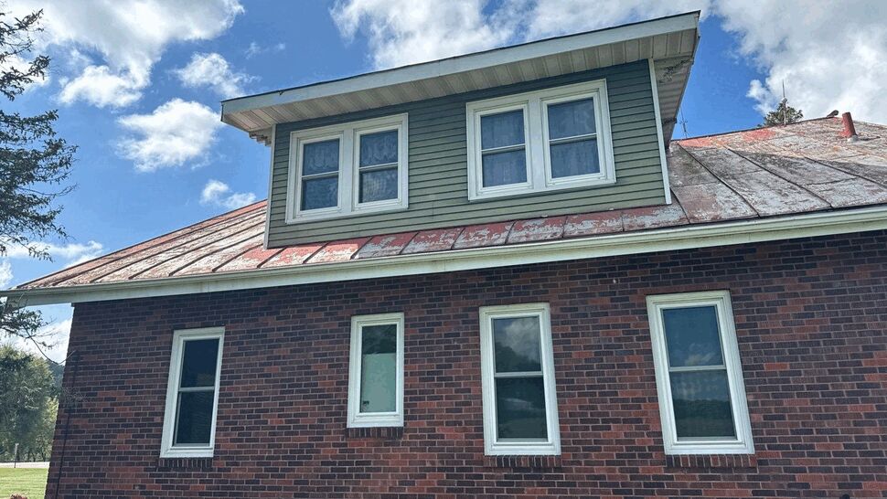 Weathered Metal Roof and Dormer | First American Roofing & Siding Inc Brick home with weathered metal roof and dormer under blue sky