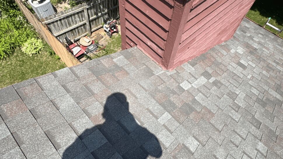 Roof shingles surrounding a chimney with a weathered masonry cap