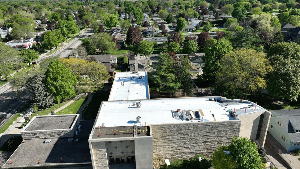 Commercial Roof Aerial View | First American Roofing & Siding Inc Aerial view of a commercial building with white flat roofing in a tree-lined neighborhood