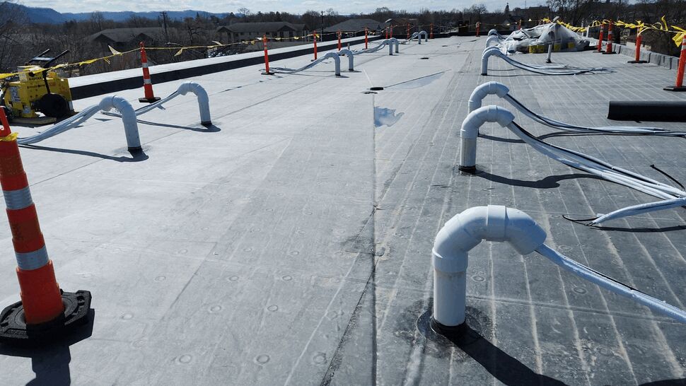 Flat commercial roof with white ventilation pipes and safety cones
