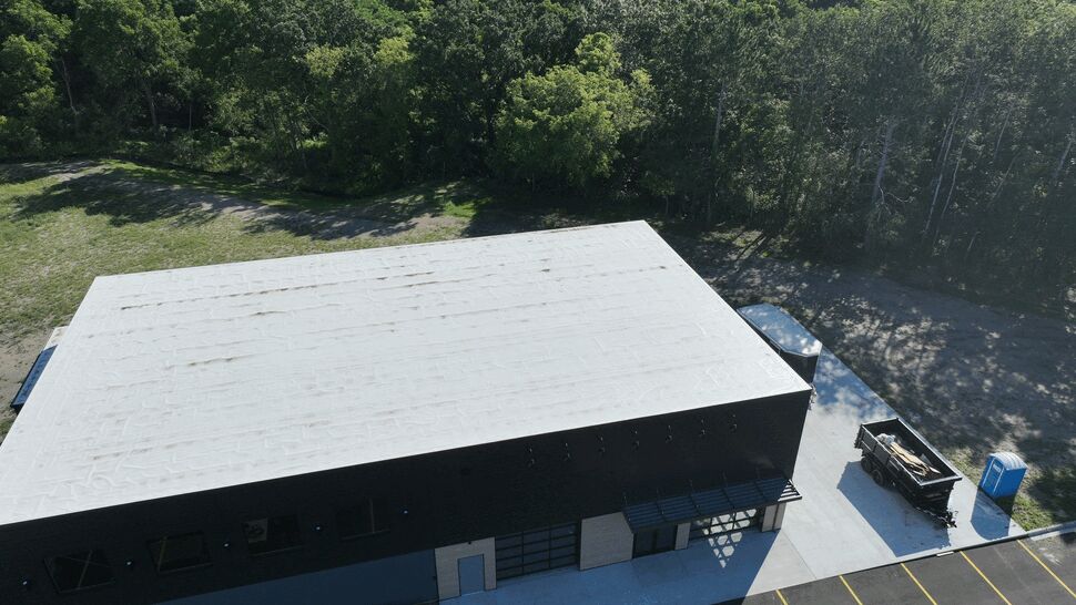 Completed Flat Roof Aerial | First American Roofing & Siding Inc Aerial view of a completed white flat commercial roof surrounded by trees.