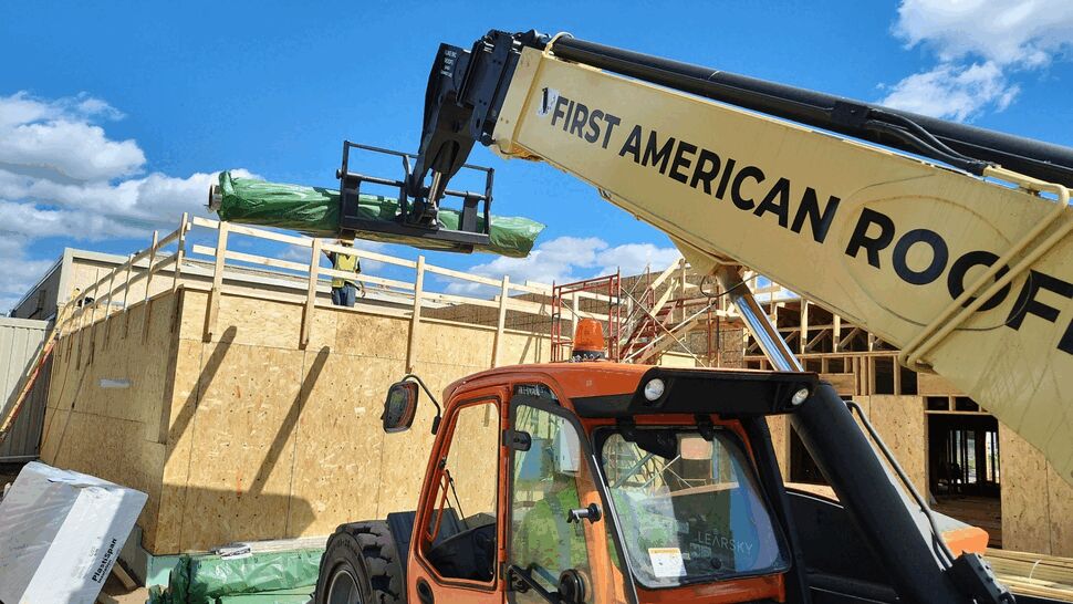 Crane boom branded First American lifting wrapped roofing materials to roof level.