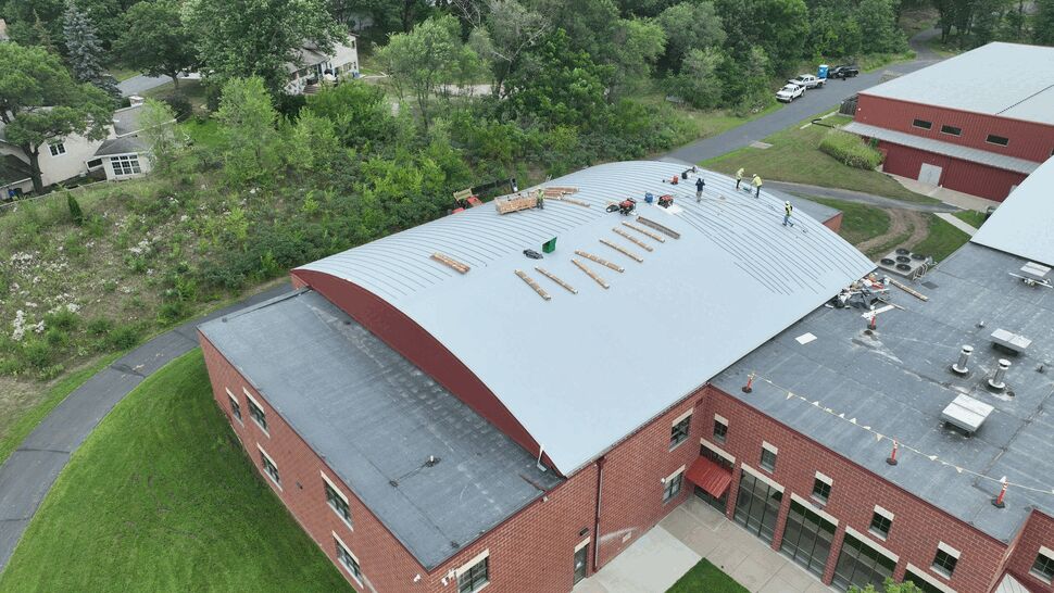Aerial view of a curved commercial roof with workers and roofing materials