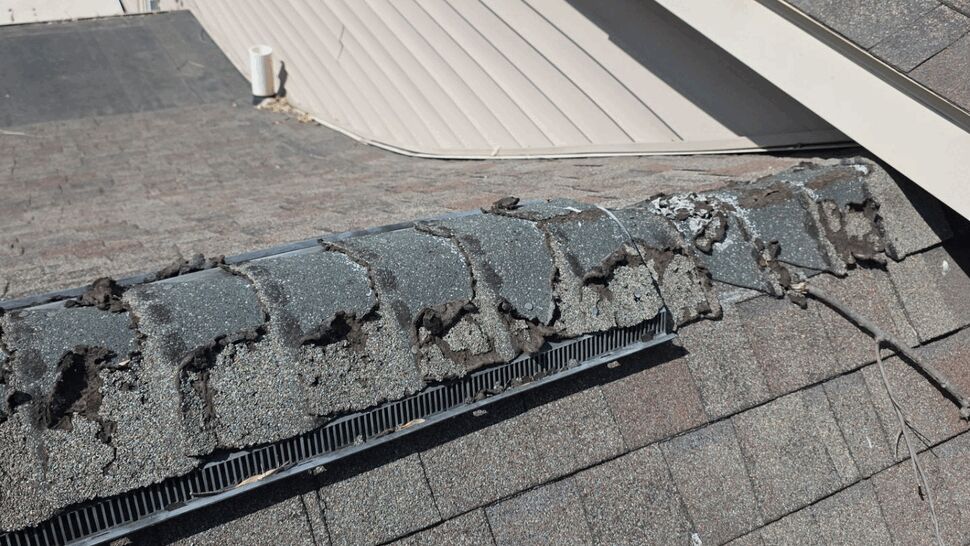 Close-up of crumbling ridge cap shingles showing deterioration and venting.