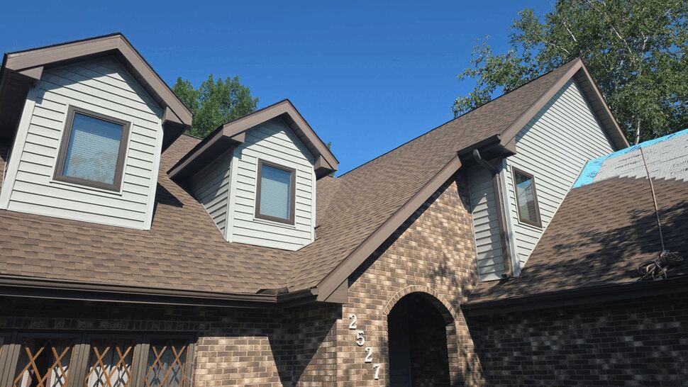 Angled view of house with dormers, arched entry, and brown roof