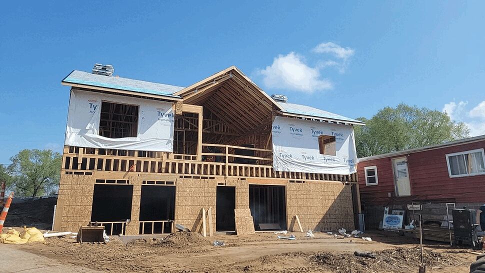 Framed home with Tyvek wrap | First American Roofing & Siding Inc Framed two-story house wrapped in Tyvek with exposed roof underlayment at a construction site.