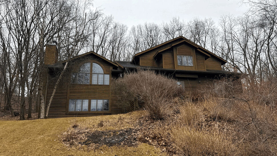Wide front view of house with multi-gabled roof and brown siding on a hill.