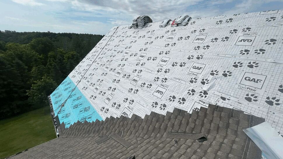 Roof deck with GAF underlayment partially covered by new shingles and shingle bundles.