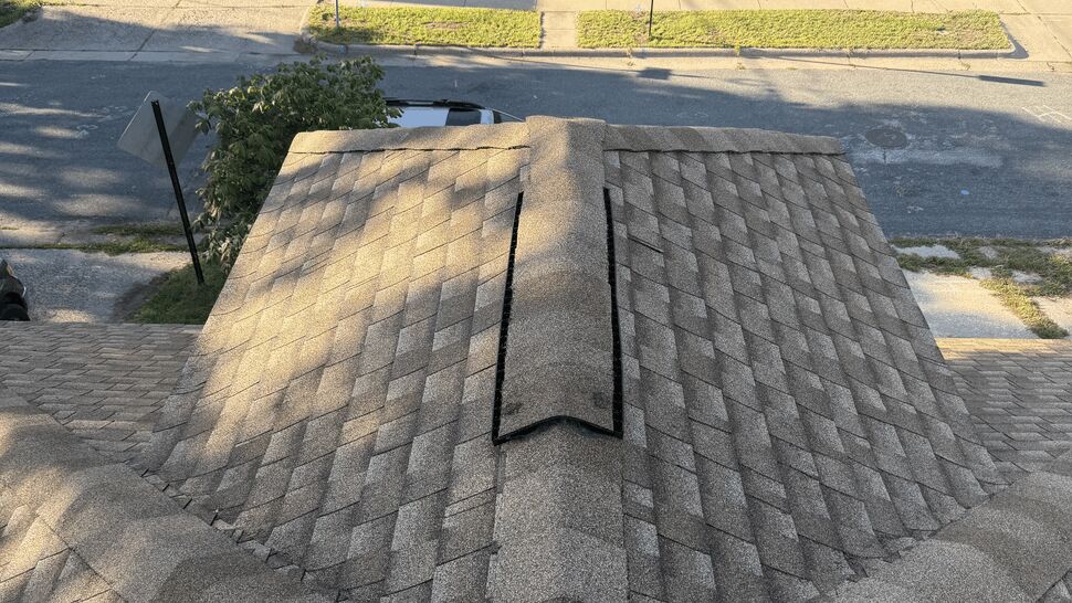 Gray asphalt shingle roof with a prominent ridge cap and residential homes beyond