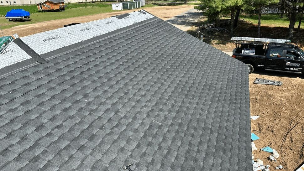 Gray shingle roof aerial | First American Roofing & Siding Inc Aerial close-up of gray asphalt shingle roof with company truck visible on the ground.