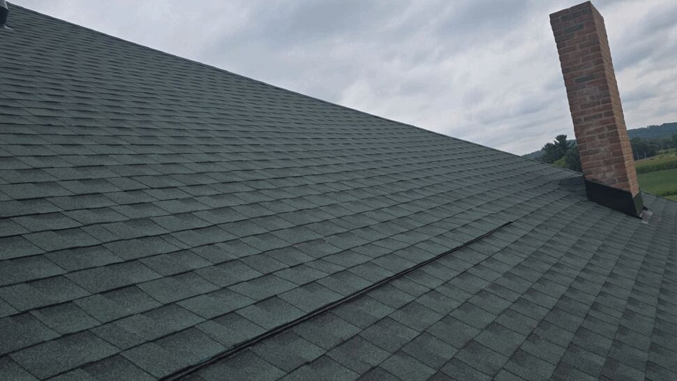 Green Shingle Roof with Chimney | First American Roofing & Siding Inc Sloped green asphalt shingle roof with brick chimney under cloudy sky
