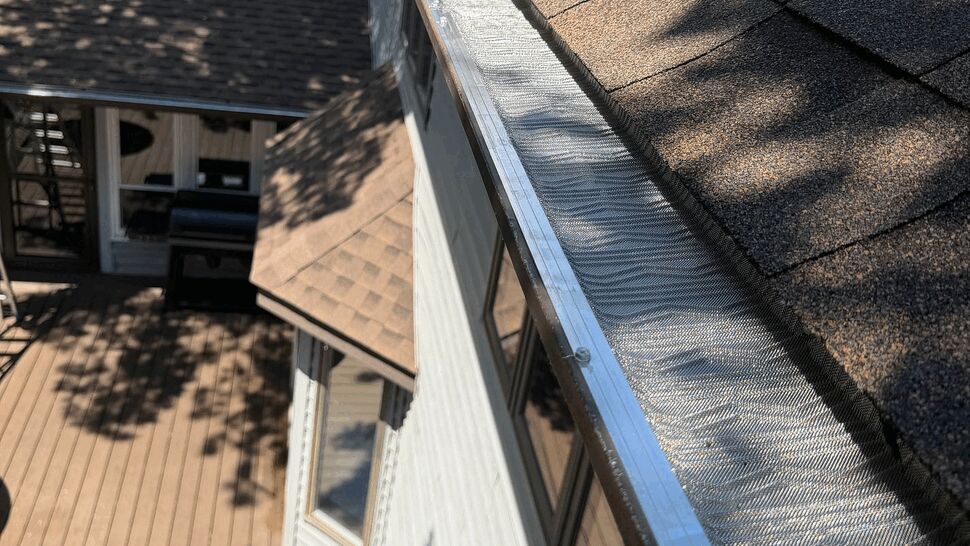 Close-up of metal gutter guard running beneath shingles along the eave