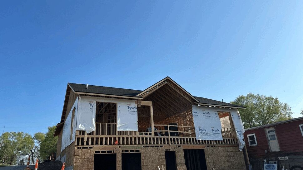 Front view of a house under construction with Tyvek wrap and a finished roof in place.