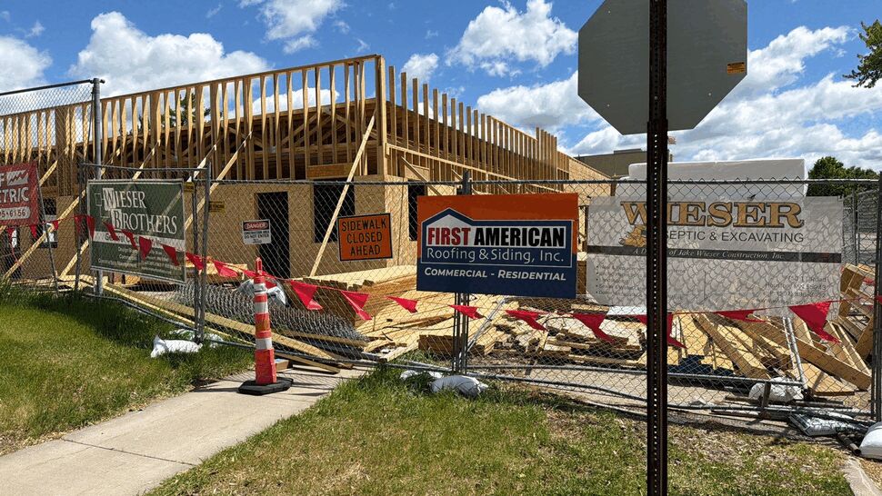 Construction site fence with First American Roofing & Siding Inc sign and wood framing.