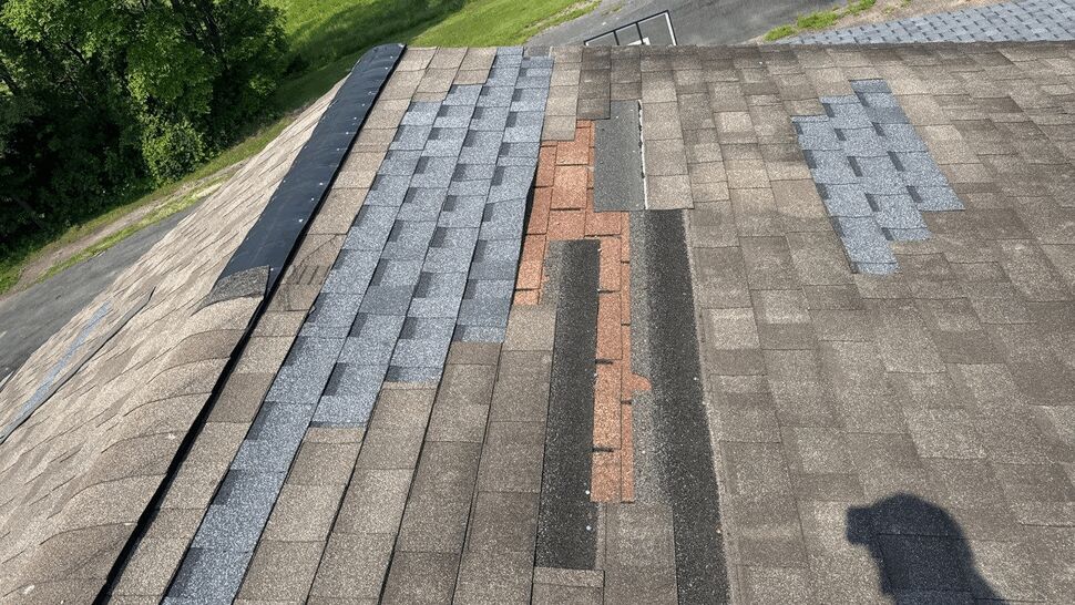Roof area with mismatched patched shingles and exposed underlayment indicating damage