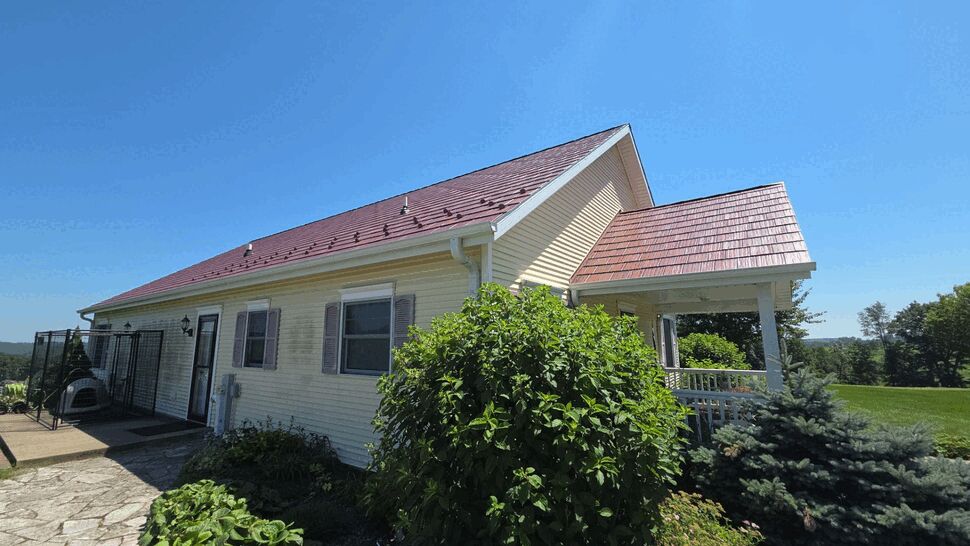 Angled porch view with red roof, gutters, and landscaped shrubs
