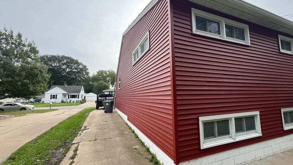 Red Vinyl Siding Exterior | First American Roofing & Siding Inc Red vinyl-sided home exterior with white trim and basement windows.