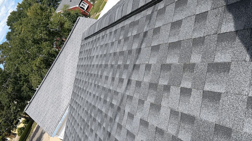 Roof Ridge Vent Detail | First American Roofing & Siding Inc Gray shingle roof with a long black ridge vent and nearby homes