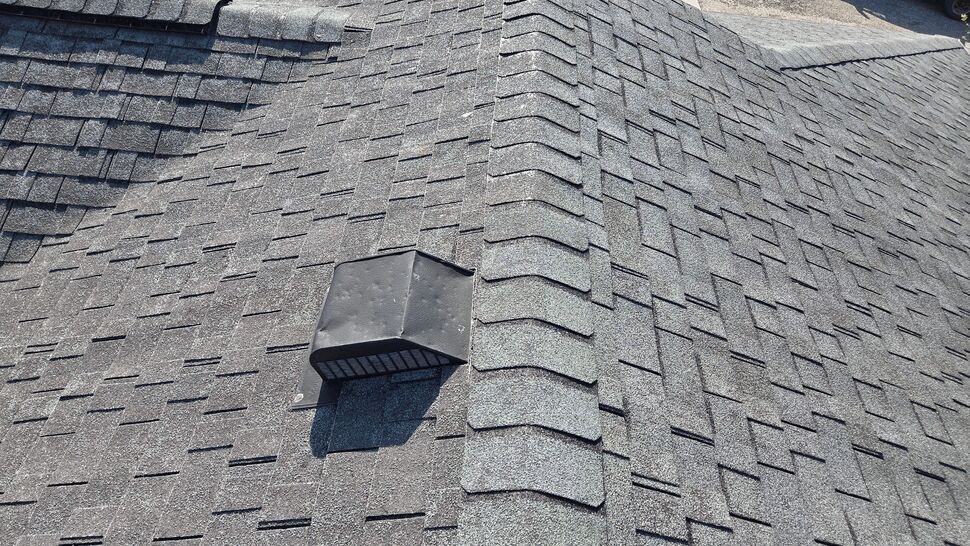 Black roof exhaust vent installed along an asphalt shingle ridge