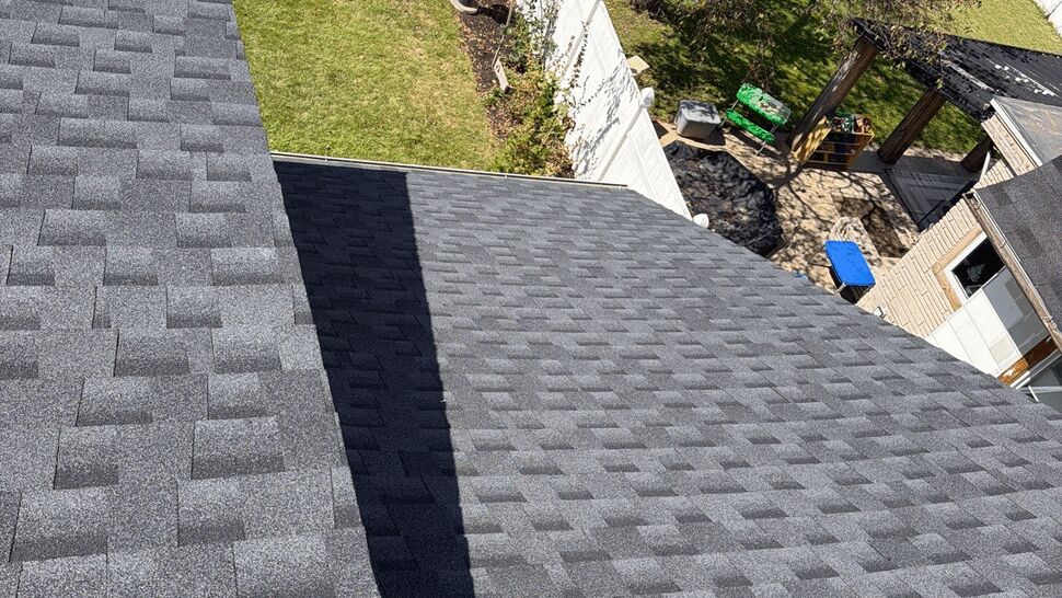 Roof Valley Shingle Detail | First American Roofing & Siding Inc Gray asphalt shingles covering intersecting roof sections beside a home