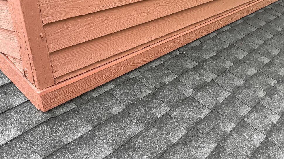 Gray roof shingles meet red horizontal siding beneath a residential window
