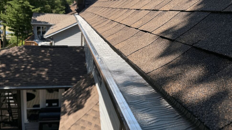 View along shingle slope with gutter guard and eave from above