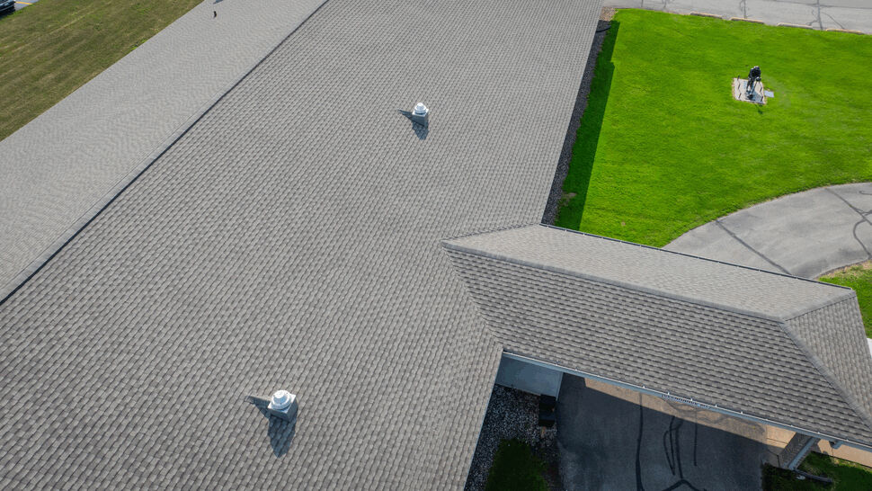 Shingle Roof Close-up with Vents | First American Roofing & Siding Inc Close-up of textured shingle roof with two white roof vents casting shadows.