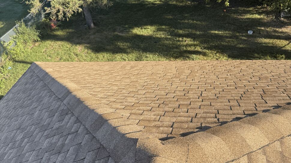 Sunlit residential roof section with tan and gray asphalt shingles