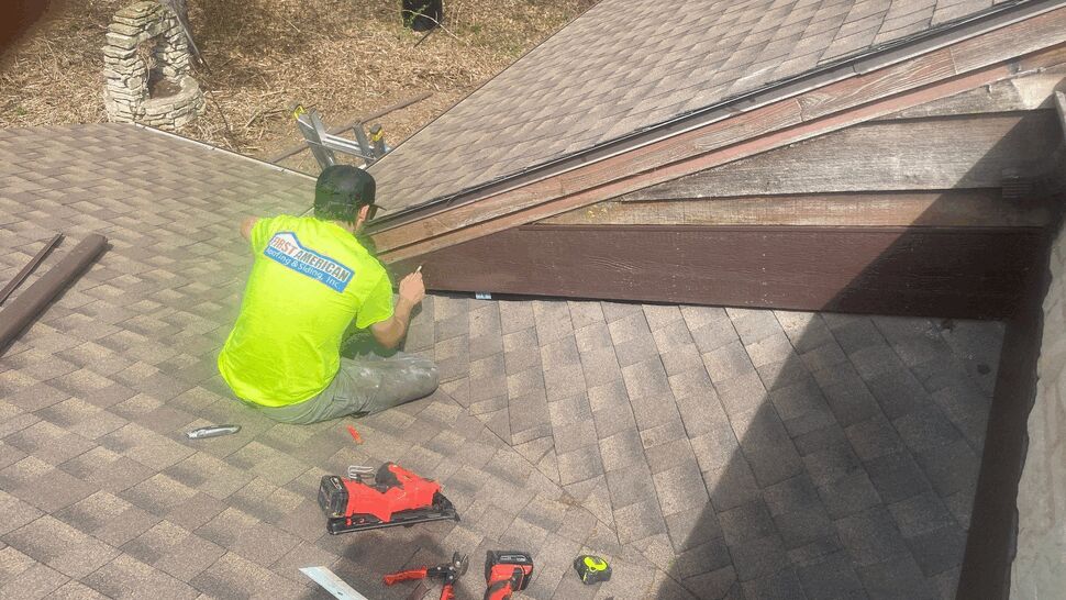Technician in a First American shirt working at the roof eave with tools on shingles.