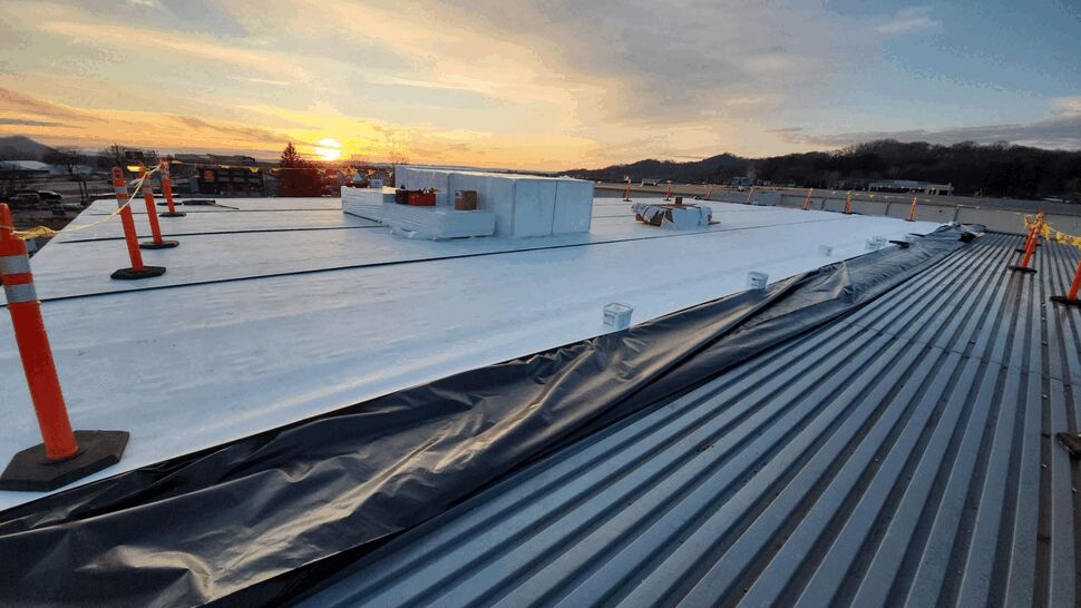 TPO Roof Installation | First American Roofing & Siding Inc Commercial rooftop under construction with white membrane, safety cones, and exposed metal decking.