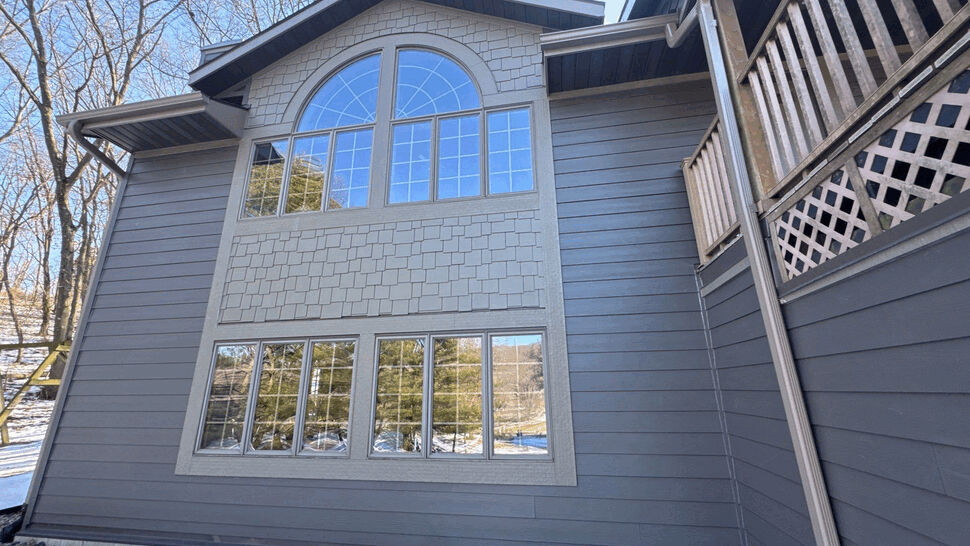 Two-story gray siding facade with large arched window and snow on the ground.