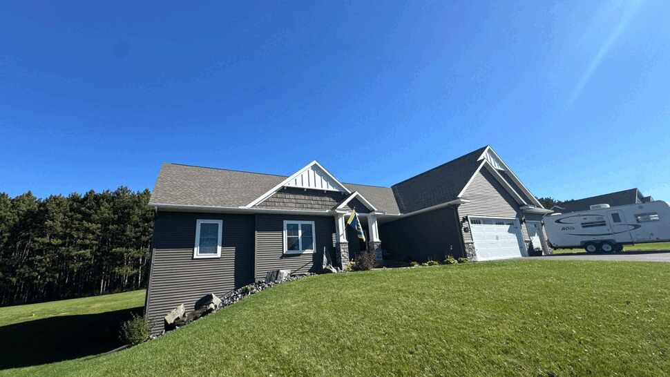 Wide view of single-story house with gray roof, garage and green lawn.