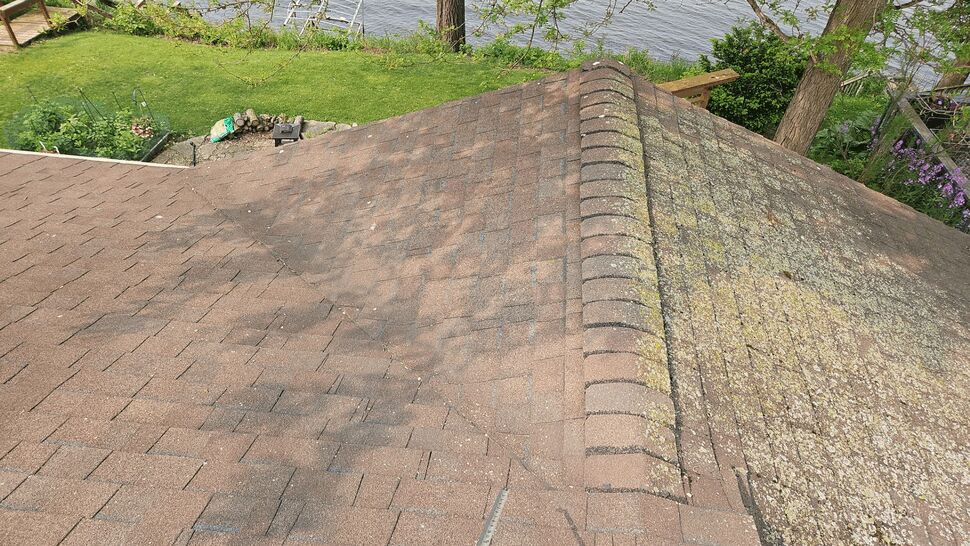 Worn roof section with moss buildup and ridge tiles overlooking a backyard and water