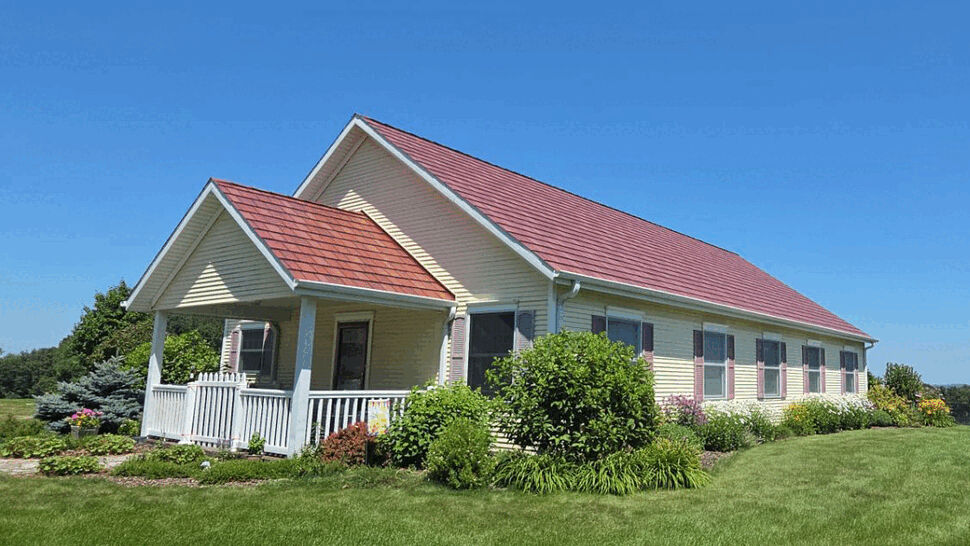 Yellow house with red roof and white porch under clear blue sky