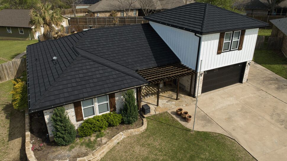 Aerial view of a house with a black metal tile-style roof and landscaped yard.